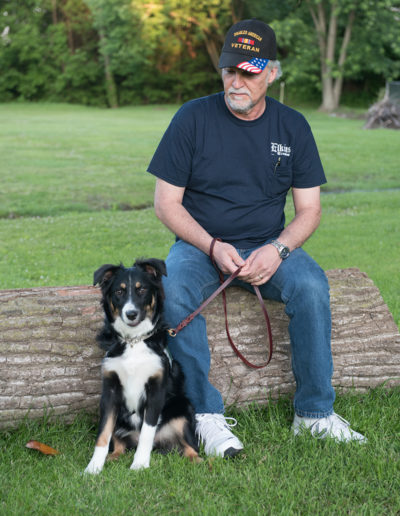 Veteran sitting on tree trunk with border collie support dog