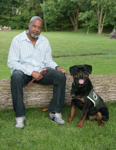 African American veteran sitting on tree trunk with rottweiler service dogs