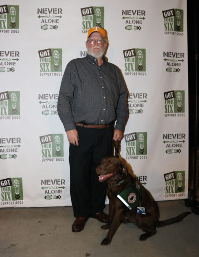 Older veteran in orange hat with chocolate lab service dog at Got Your Six Support Dogs graduation ceremony